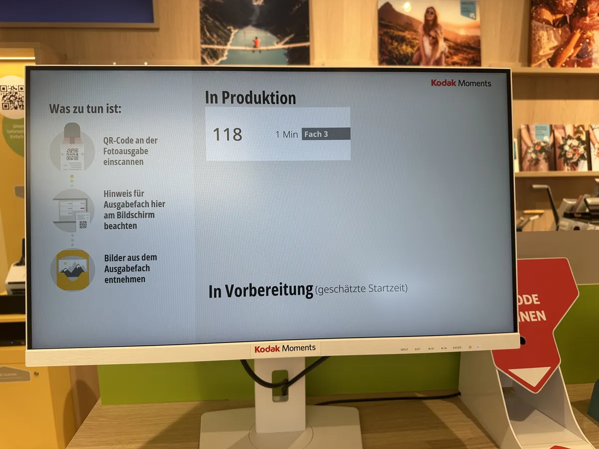 Kodak Moments Bildschirm zeigt: In Produktion — Bestellung 118, 1 Minute geschätzte Zeit, Ausgabe in Fach 3.